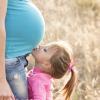 Daughter kissing her mum's pregnant belly