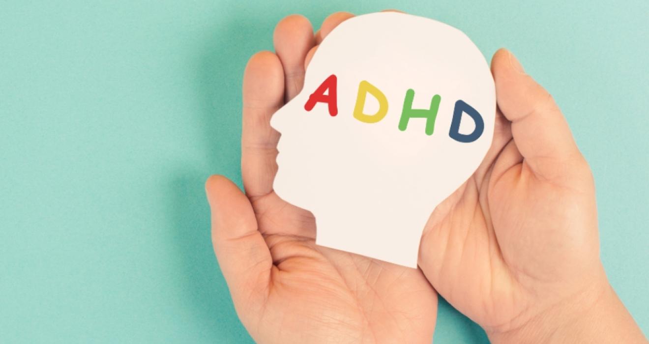 picture of a childs hands holding a cut out of a childs head with the letters ADHD written on