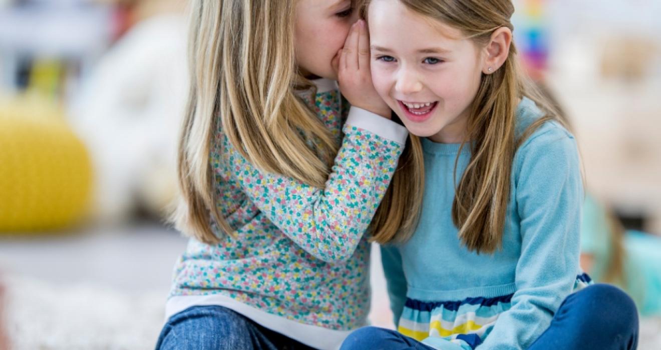 picture of two primary school children whispering to eachother while learning about friendship