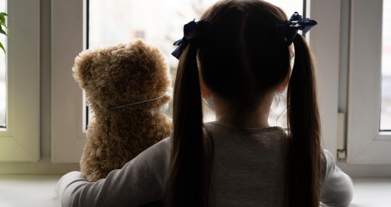 picture of a sad child with a teddy looking out of the window