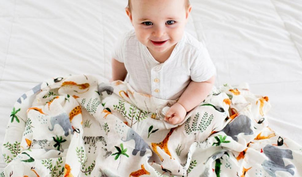 a happy baby sitting under an animal themed Loulou Lollipop blanket picture of a happy baby sitting under an animal themed Loulou Lollipop blanket