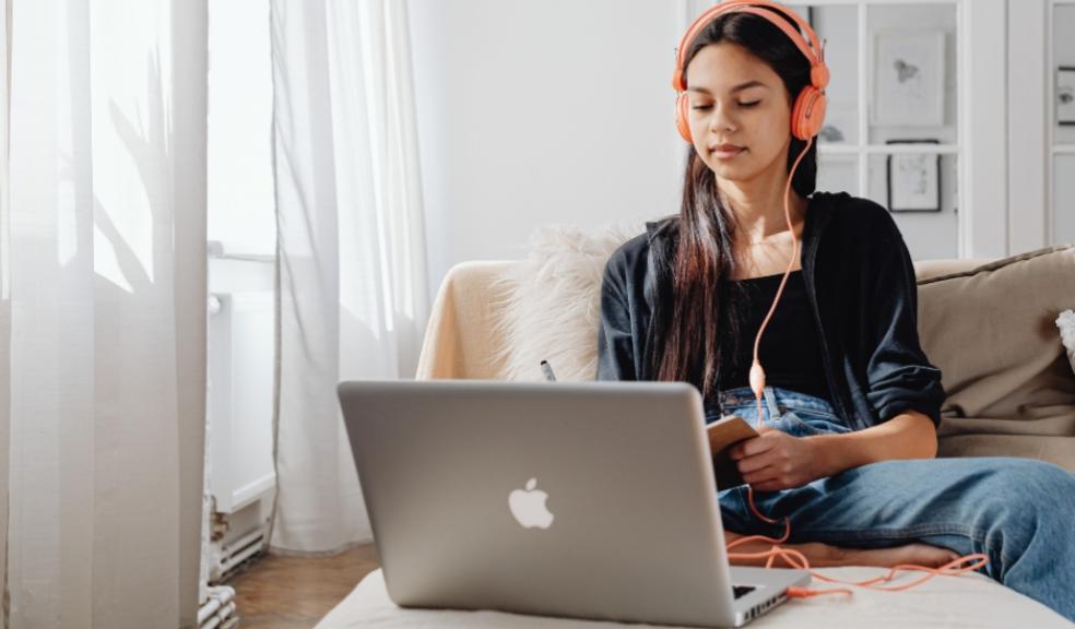 picture of a girl watching YouTube on her apple laptop whilst wearing orange headphones