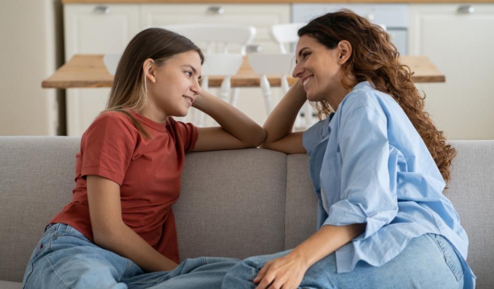 picture of a happy parent sat on a sofa talking to her teenage daughter