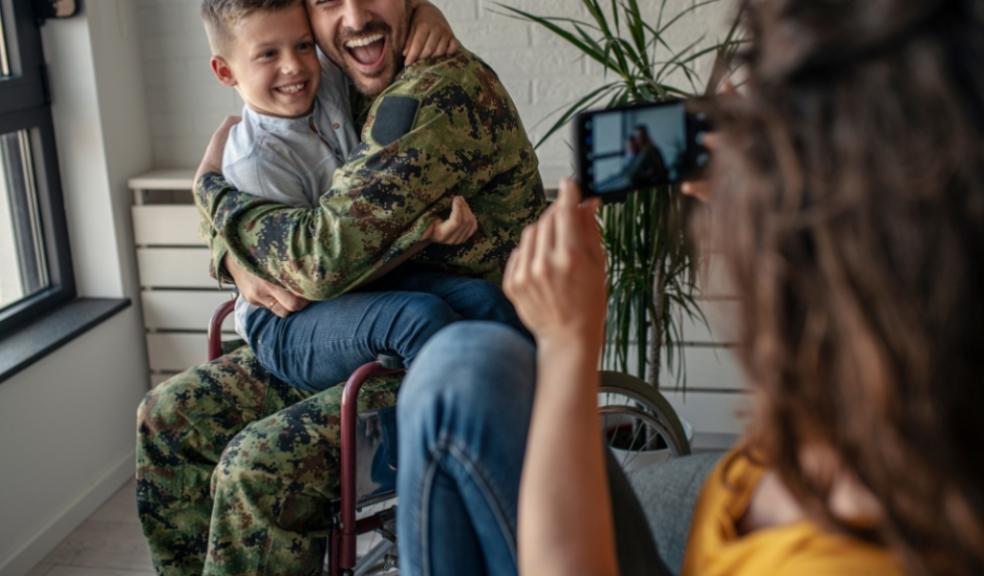 picture of a woman taking a photo of a military veteran in a wheelchair with child on his lap
