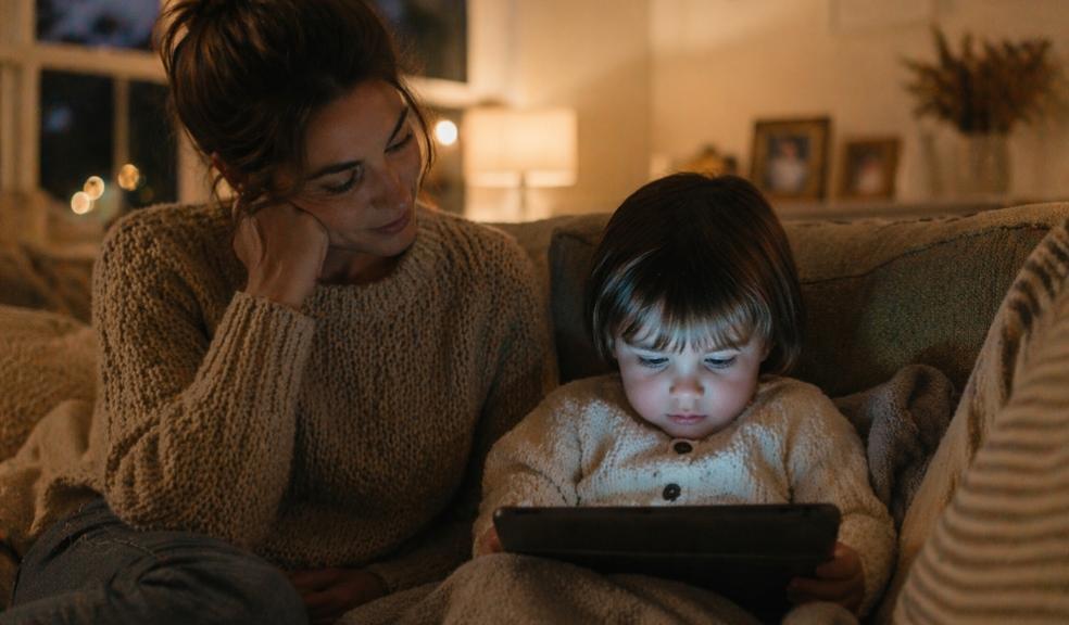 picture of Toddler watching a tablet on the sofa in a dimly lit living room while parent sits nearby, showing evening screen time before bed