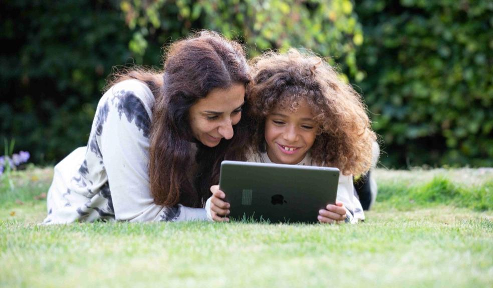 picture of a happy mum and child laying on grass playing on the doodle maths app on an ipad