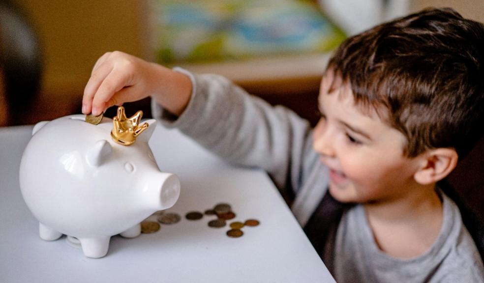 picture of a child putting money in a white piggy bank