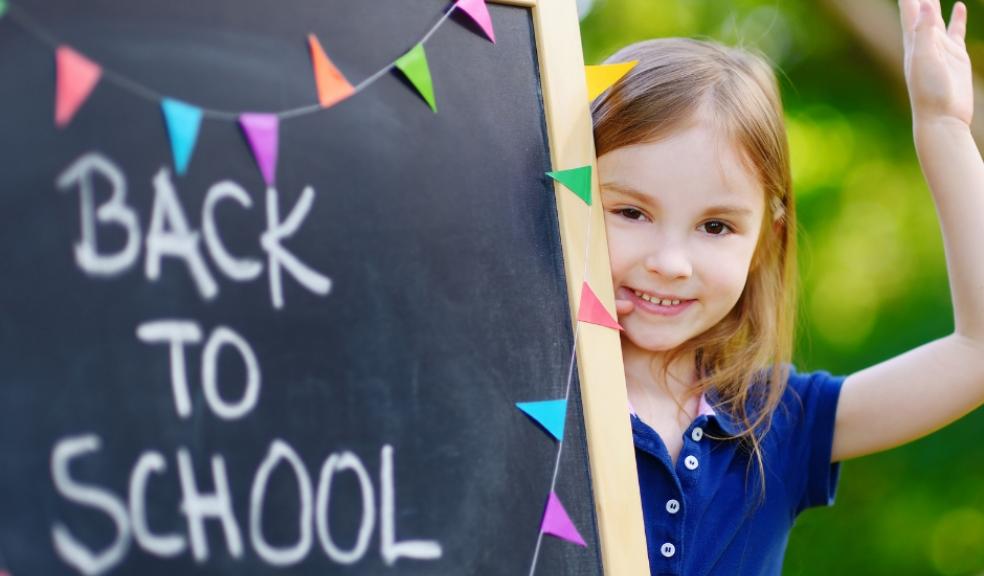 Picture of girl stood next to a chalkboard with back to school written on it