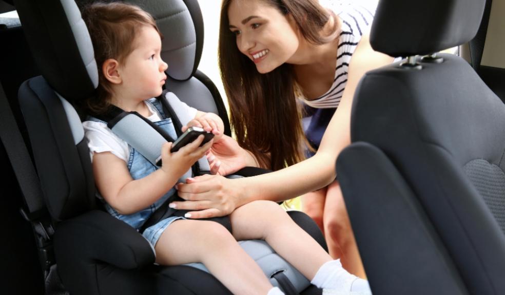 picture of a mum strapping her child into a car seat with a mobile phone