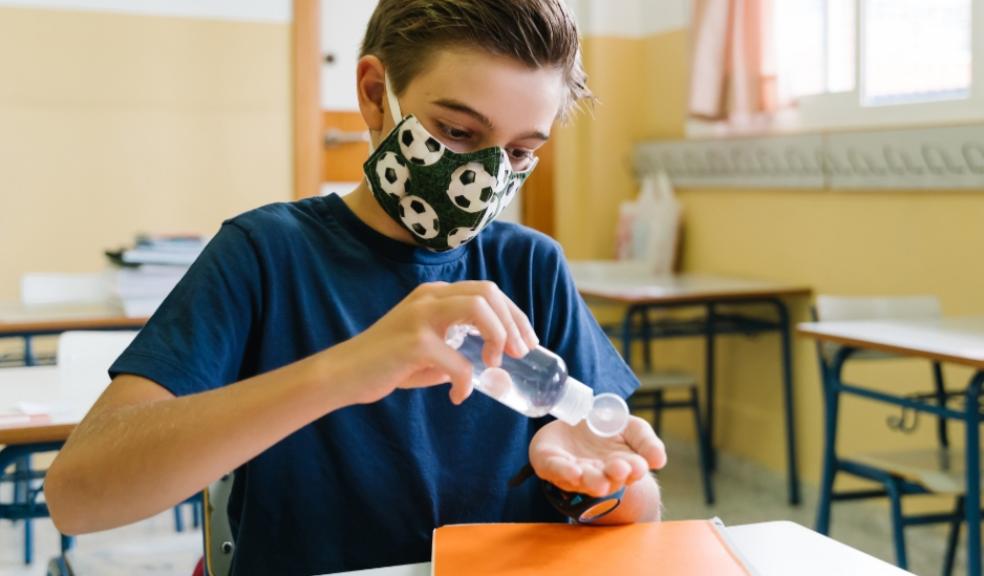 picture of a child wearing a face mask and using hand sanitiser in a school classroom