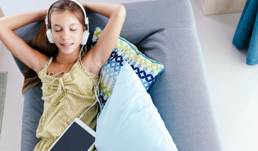 picture of a child laying on the sofa with headphones on and a tablet device