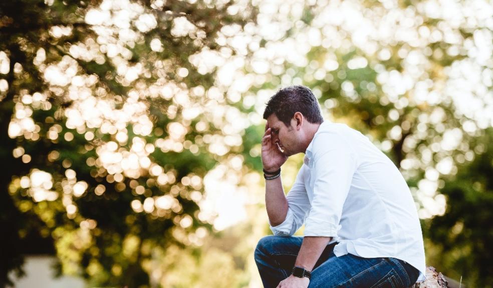 Picture of a man sat outside in the sunshine with his head in his hands