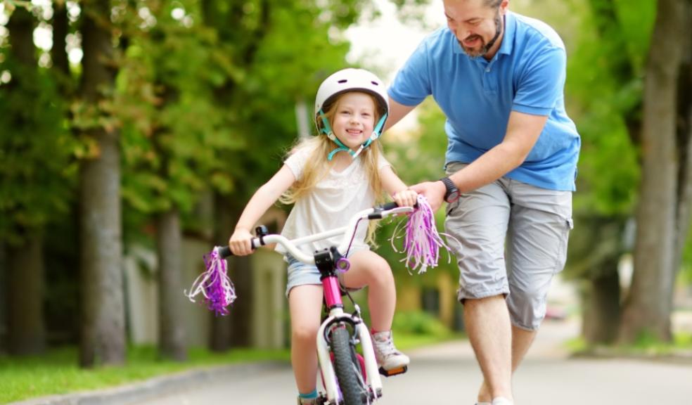 picture of a dad helping daughter learn how to ride a bike