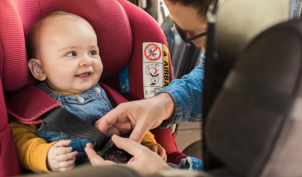 picture of a dad putting a happy baby in a red car seat