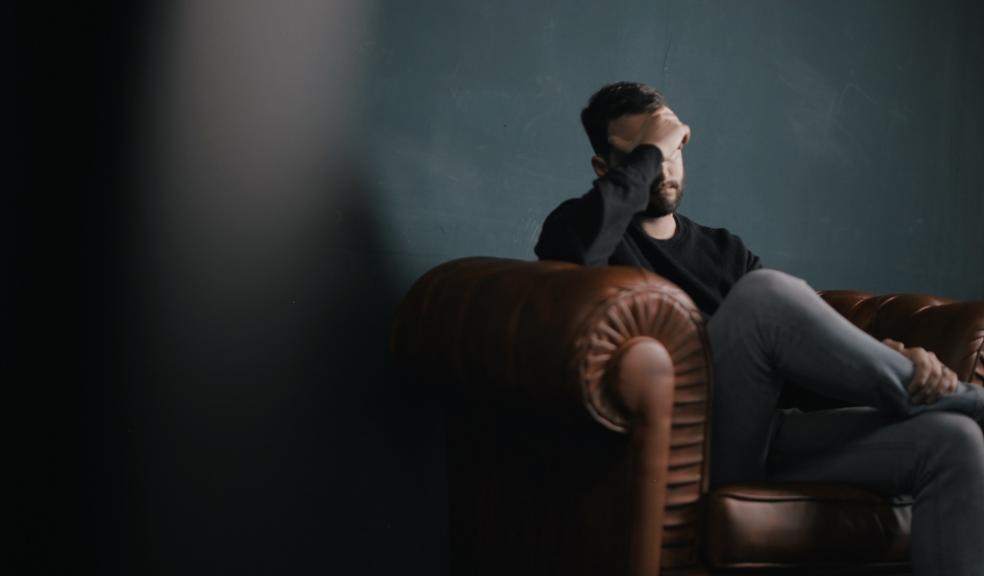 Photo of a man sat on a sofa with his head in his hands