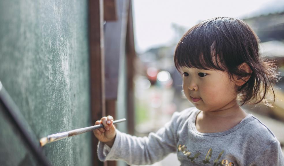 Picture of a little girl painting a fence outside