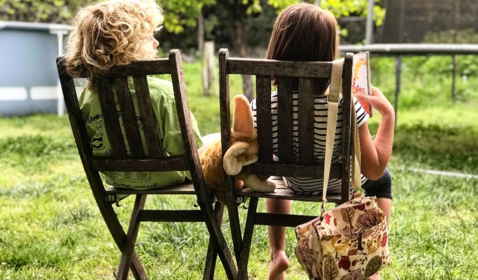 picture of a boy and girl sat on chairs reading a book in the garden