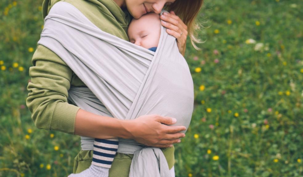 woman with a baby sleeping in a sling outdoors in nature picture of a woman with a baby sleeping in a sling outdoors in nature