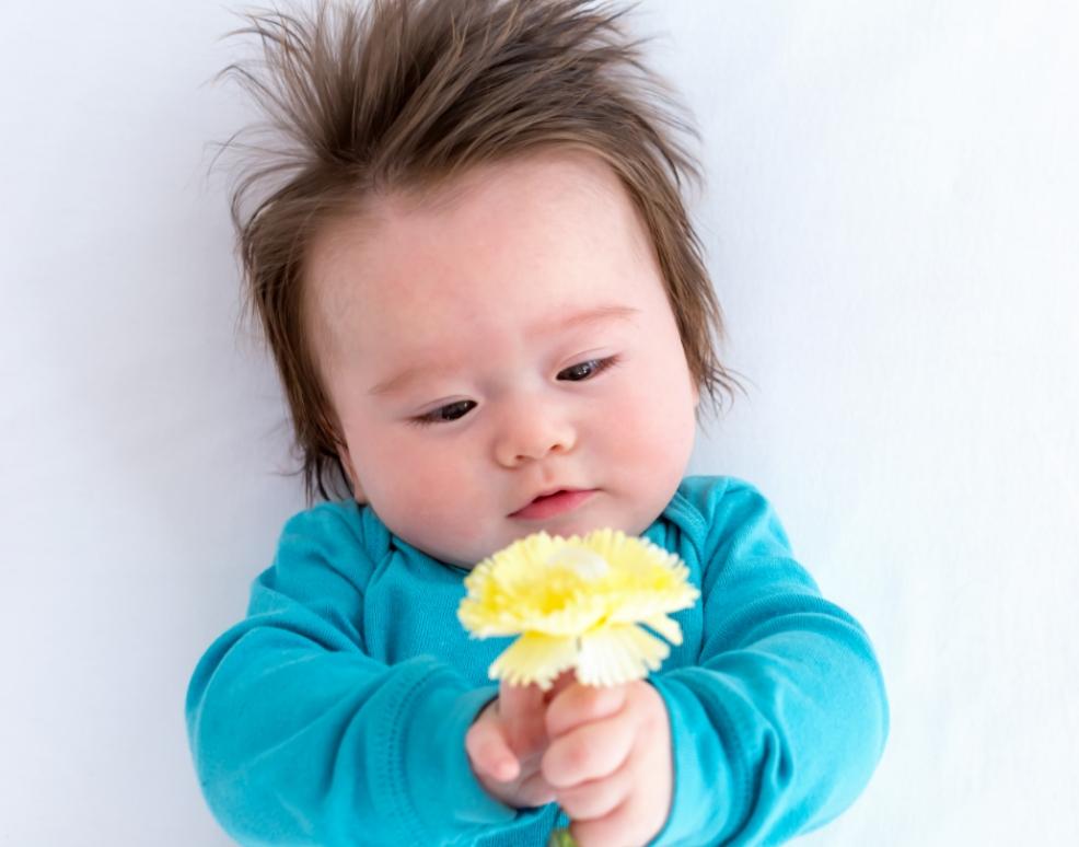 picture of a cute baby wearing blue holding a yellow flower