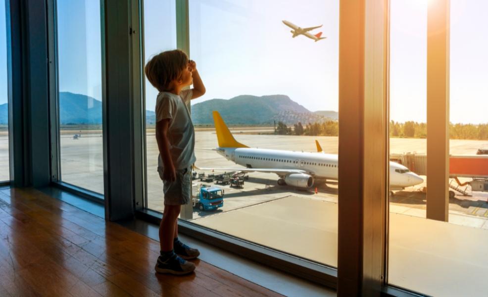 picture of a boy looking out of an airport window at sunny aeroplanes