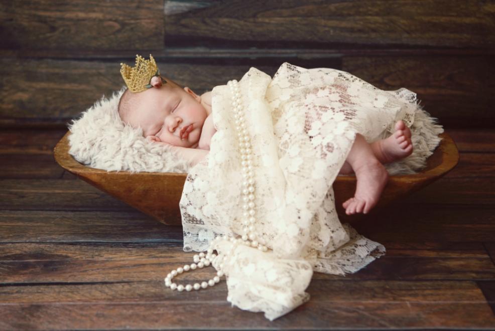 picture of a baby wearing a crown, wrapped in a lace blanket and pearls