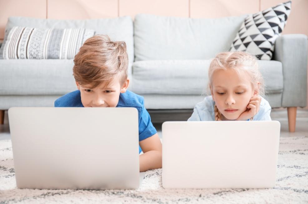 picture of boy and girl child laying on the living room floor on their laptops