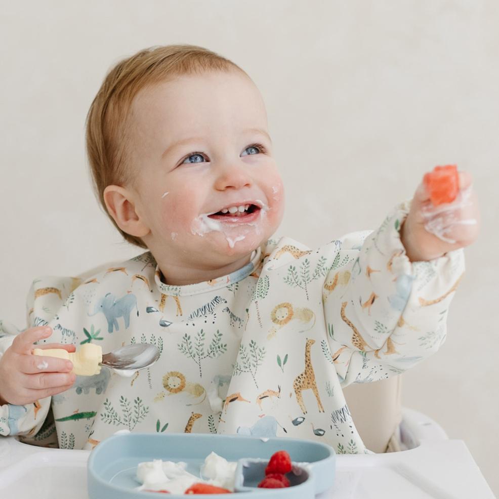 a happy baby weaning using the Loulou Lollipop bib cuttlery and plate set picture of a happy baby weaning using the Loulou Lollipop bib cuttlery and plate set