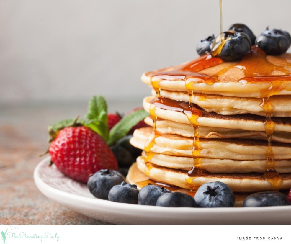 picture of a stack of pancakes served with strawberries blueberries and maple syrup