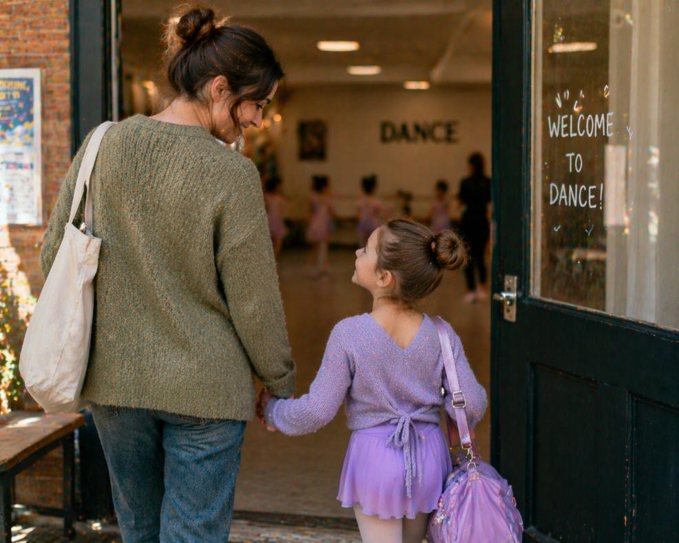 picture of Mother holding her daughter’s hand as they walk into a dance studio, with the child dressed for ballet and looking excited