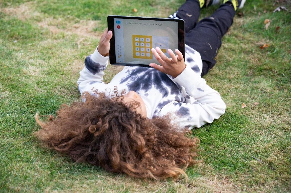 picture of A child laying on the grass playing on the Doodle app on a device