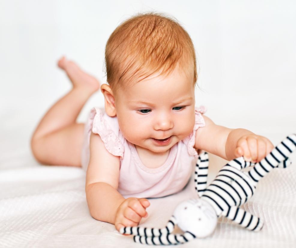 picture of a baby on her tummy playing with a black and white cuddly toy