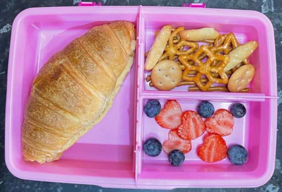picture of a childrens lunchbox with a cheese croissant fruit and pretzels