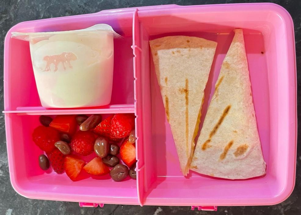 picture of a childrens pink lunch box with cheese quesadilla fruit and yoghurt