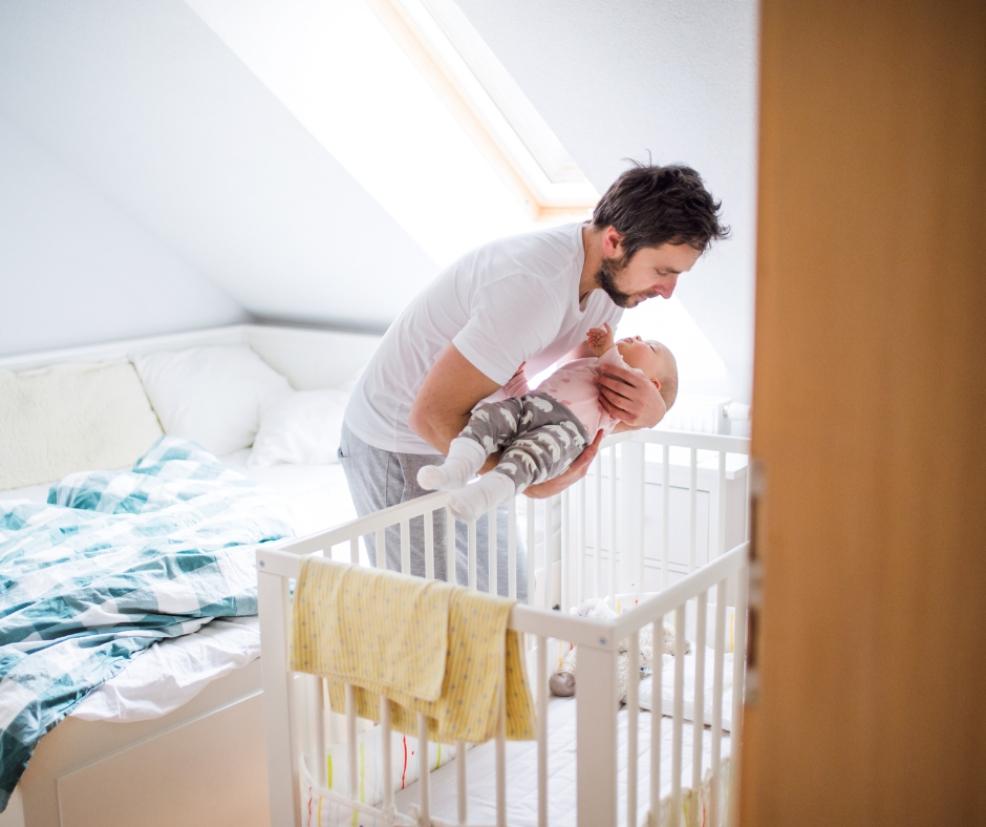 picture of a dad putting a sleeping baby in their cot