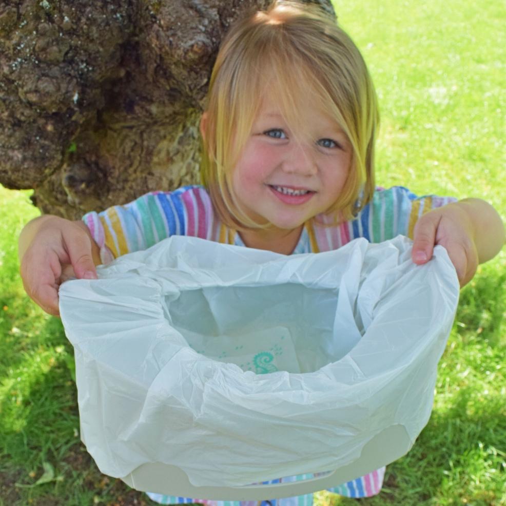 picture of a child holding up a potette potty with liner ready to use outside