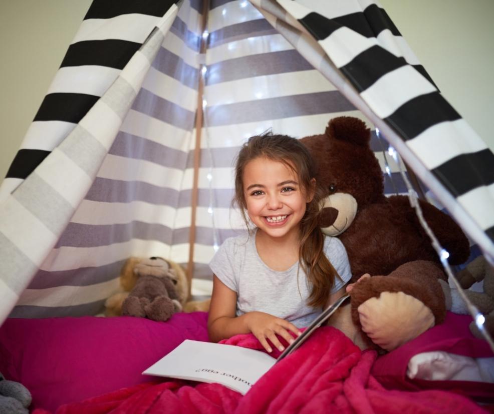 picture of a happy child in a wigwam reading with blankets