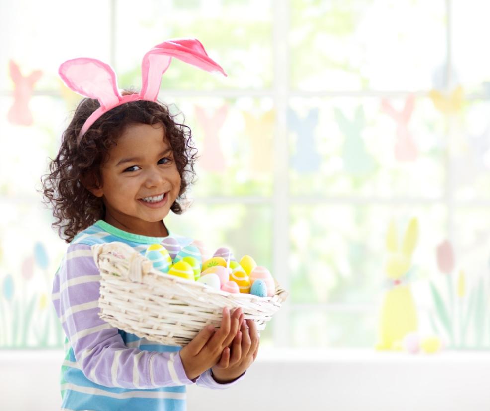 picture of a happy child wearing bunny ears holding a basket of easter eggs