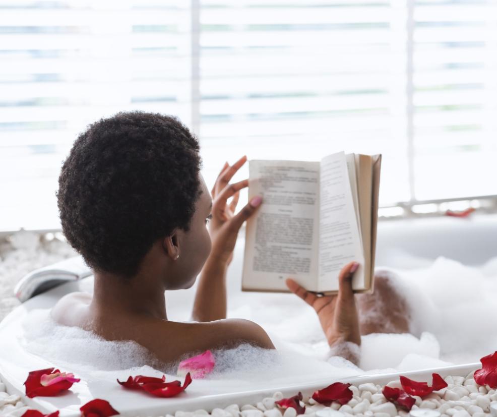picture of a woman relaxing by reading in a bath with rose petals