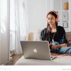picture of a girl watching YouTube on her apple laptop whilst wearing orange headphones