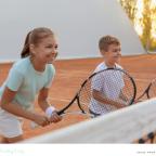 picture of two happy children on a tennis court with tennis rackets having a lesson