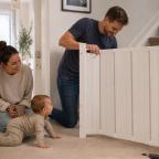 picture of Dad fitting a stair gate while a mum and crawling baby watch nearby in a family home, showing babyproofing and home safety in action
