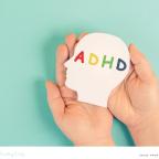 picture of a childs hands holding a cut out of a childs head with the letters ADHD written on
