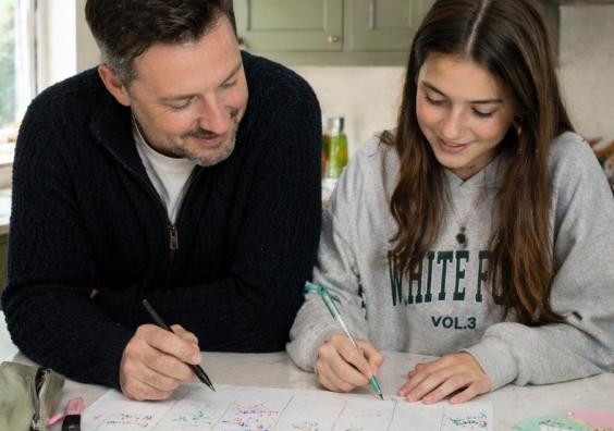 picture of Dad helping his teenage daughter create a revision timetable at a kitchen island in a bright family home