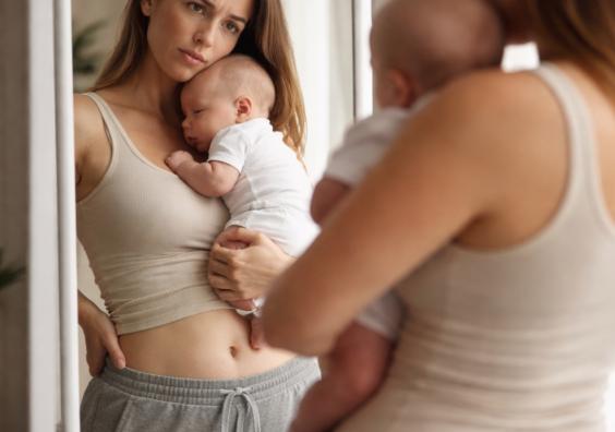 picture of New mum holding baby while looking at her reflection in a mirror representing postpartum body image and motherhood