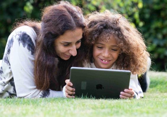 picture of a happy mum and child laying on grass playing on the doodle maths app on an ipad