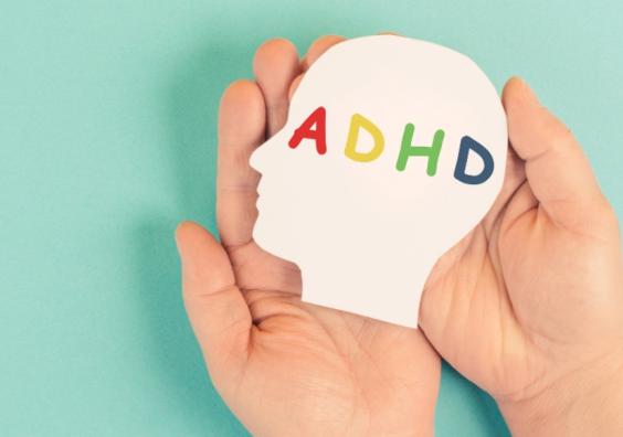 picture of a childs hands holding a cut out of a childs head with the letters ADHD written on