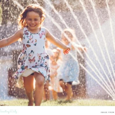picture of a happy child running through a sprinkler on a hot summer day in the garden
