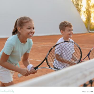 picture of two happy children on a tennis court with tennis rackets having a lesson