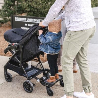 picture of parent using a lascal buggy board to walk toddler and baby to school