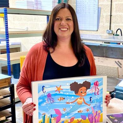 Founder of Play Shed Puzzles, Jacqueline Buckland is in the jigsaw factory holding a mermaid puzzle 